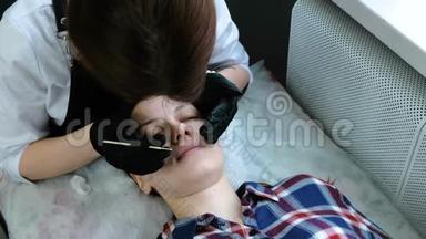 美容师用棉签擦拭病人`眼睑。 睫毛层压板。 美容治疗。